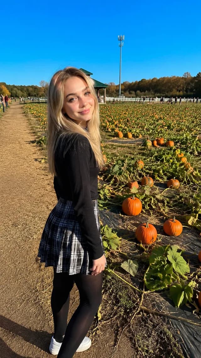 Woman in a black top and plaid skirt browsing a pumpkin patch on an autumn day