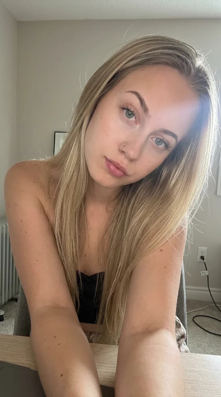 Woman in a black top leaning over a desk taking a close-up selfie